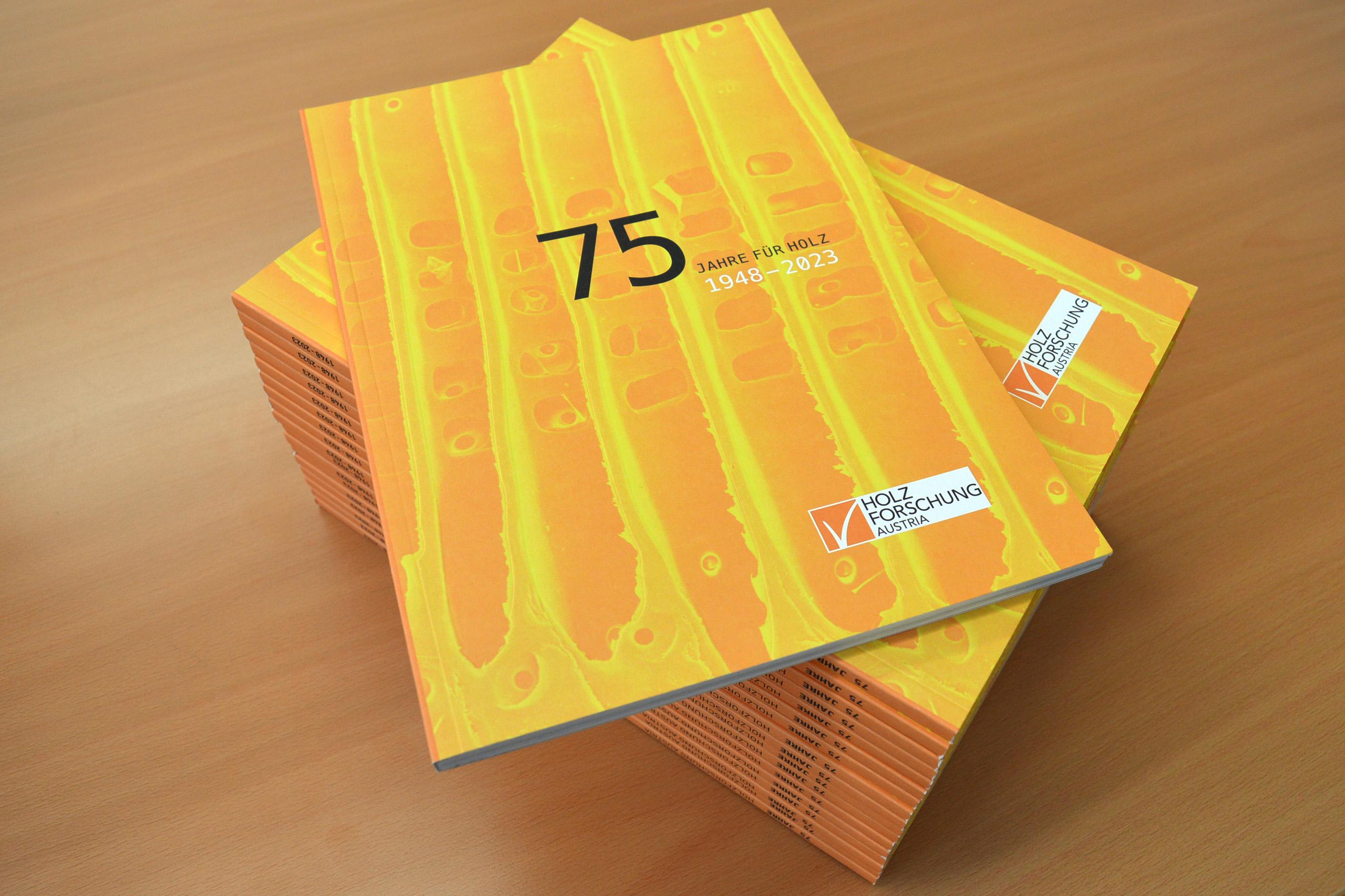 A stack of the commemorative publication 75 Years of Wood Research Austria lies on a wooden table.