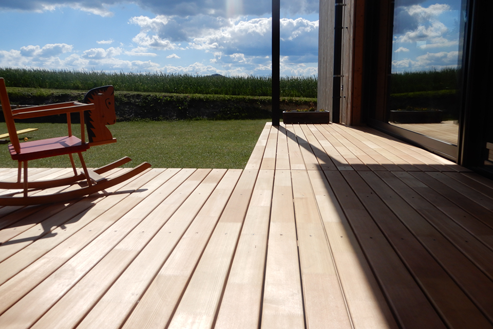 A wooden terrace with a rocking horse standing on it, backlit by the sun.